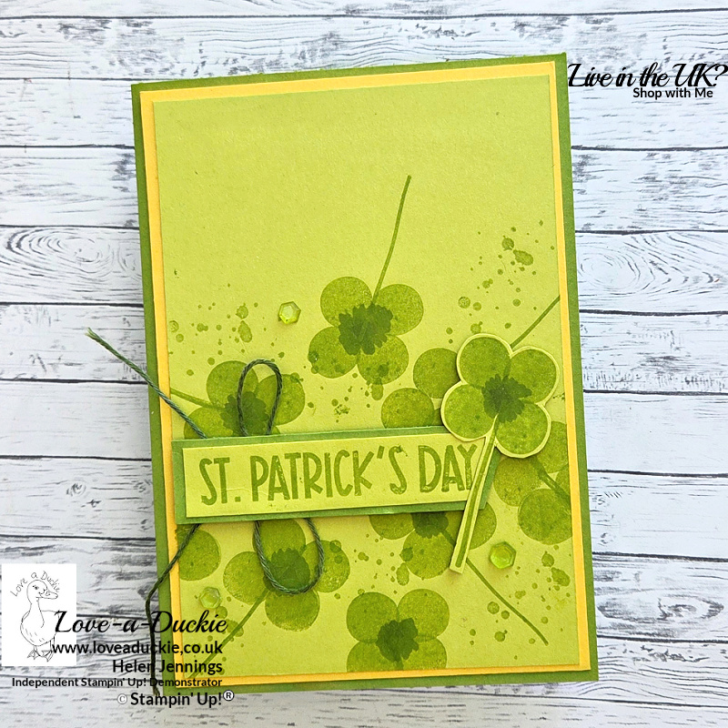 Handmade St. Patrick’s Day card featuring stamped four-leaf clovers in Granny Apple Green with layered yellow mats, twine detail and green gems created for the Festive Friday Challenge.